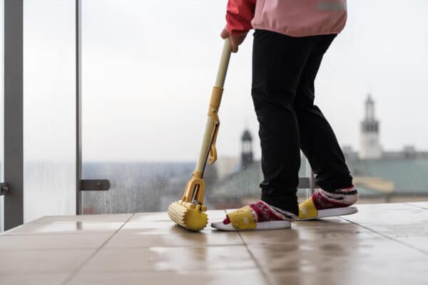 Preschool age girl cleaning balcony floor with mop. Spring cleaning concept.