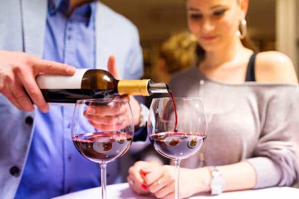Close-up of red wine being poured into glasses during a cozy couple’s night at home.